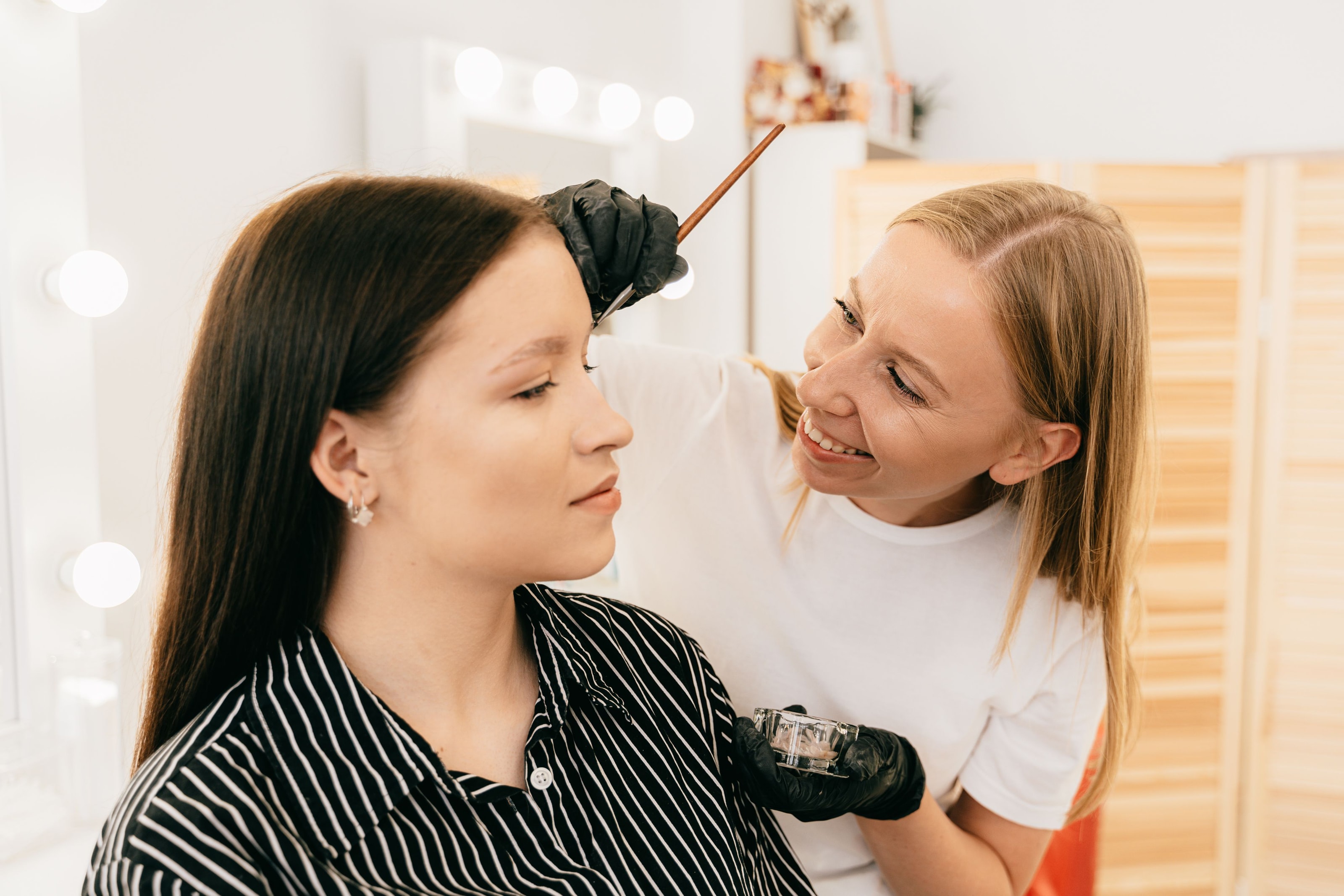 A smiling brow artist applying tint to a customer's brows